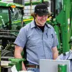 High-quality green John Deere agricultural machinery at JCE AG, with two smiling technicians working together in a well-equipped farm equipment dealership.