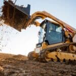 Excavator with a front loader clearing dirt and debris on a construction site at sunset.