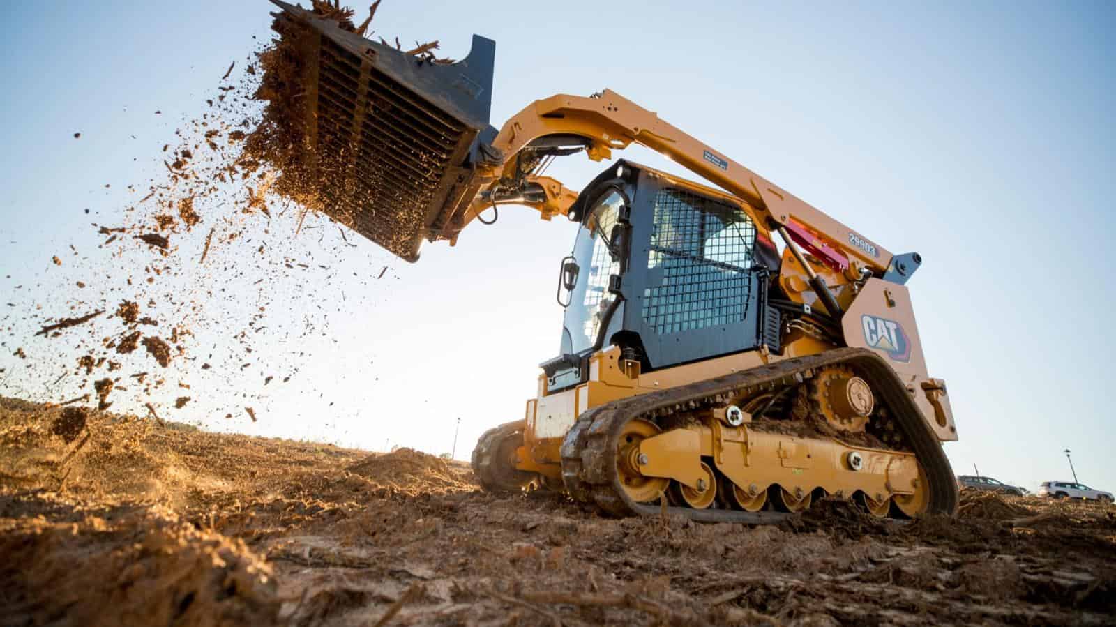 Excavator with a front loader clearing dirt and debris on a construction site at sunset.