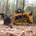 Heavy-duty CAT compact track loader clearing forest debris in woodland environment.