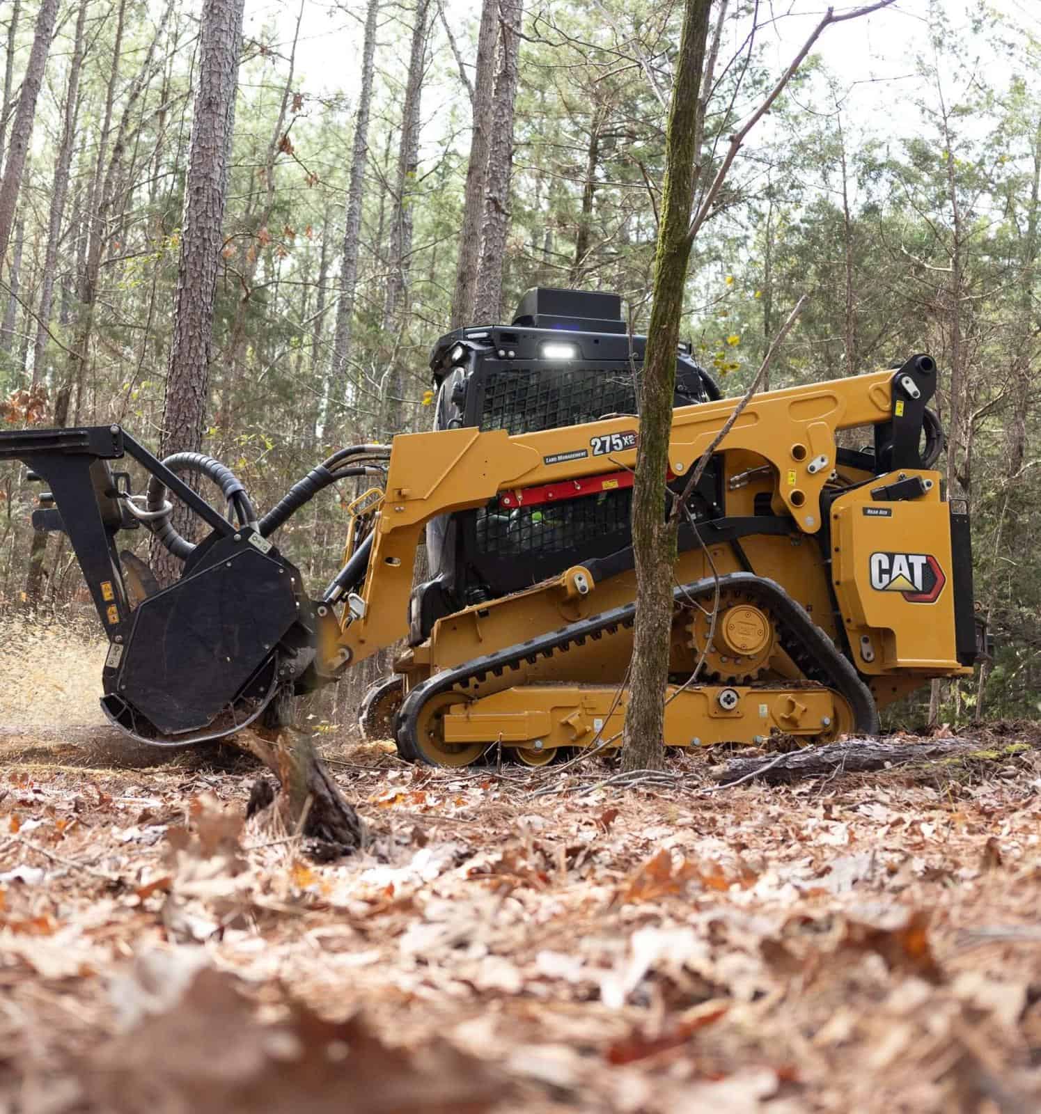 Heavy-duty CAT compact track loader clearing forest debris in woodland environment.